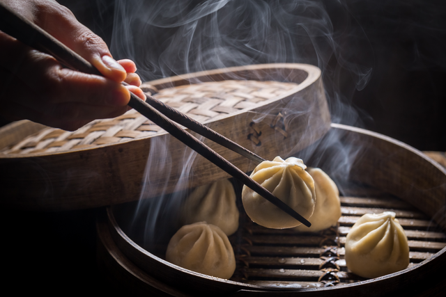 Dumpling being taken out of a steaming basket with chop sticks.